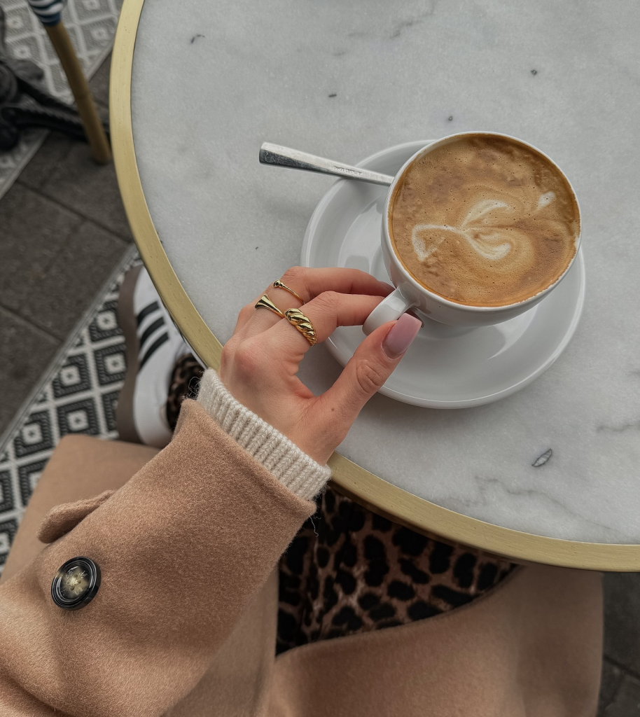 Aesthetic picture of a coffee mug with latte and a hand with a sweater holding the mug.